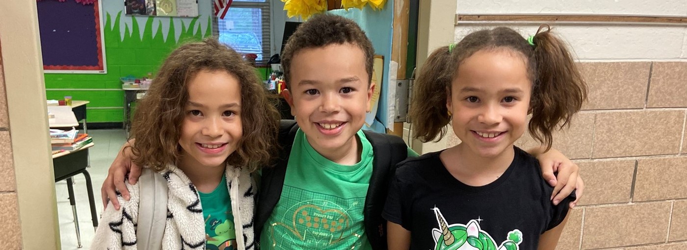 Triplets-one boy and two girls smiling wearing green