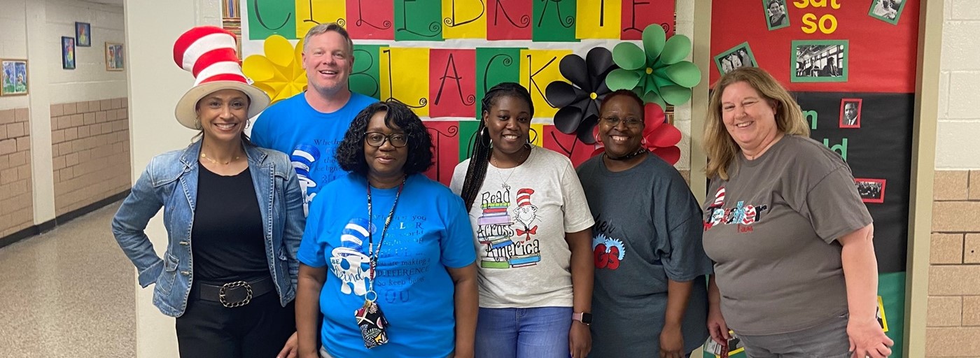 six teachers standing in front of a bulletin board smiling on read across America day